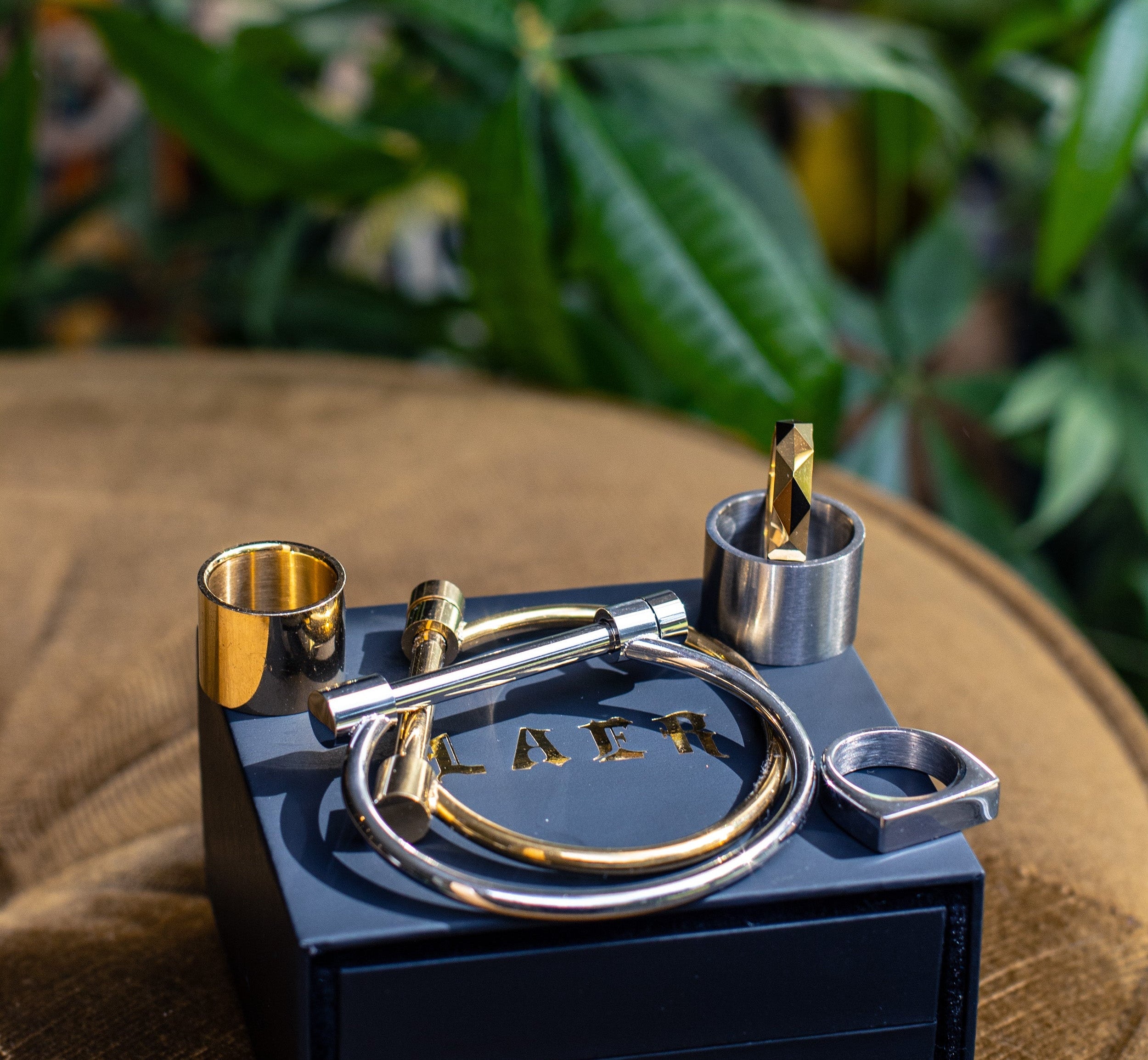 Black and gold jewelry set on a wooden surface with green leaves in the background
